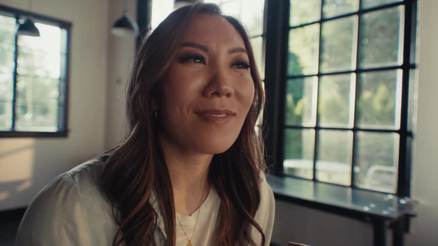 An asian woman sits in a cafe and smiles while holding a book