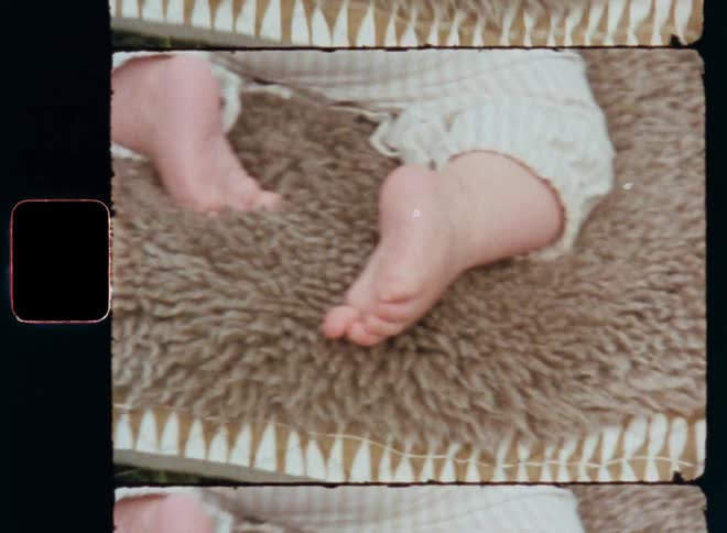 Close up of baby’s feet lying face down on rug or blanket and soft fur of a sheepskin training or learning to move and wiggling around while crawling over the ground or floor on retro home movie film footage