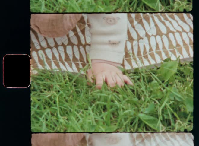 Young child or toddler crawling on a picnic blanket with his tiny baby hand touching or grabbing green grass experiencing tactile impressions and connection to nature while developing the sense of touch during early childhood captured on vintage S8 film