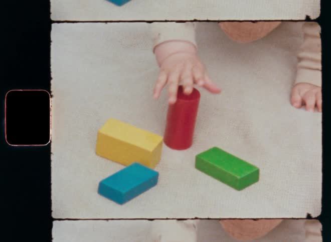 Baby girl or boy crawling towards his or her toys while playing and successfully grabbing the red toy block or building brick with his hand before lifting it up in the air with excitement and fun