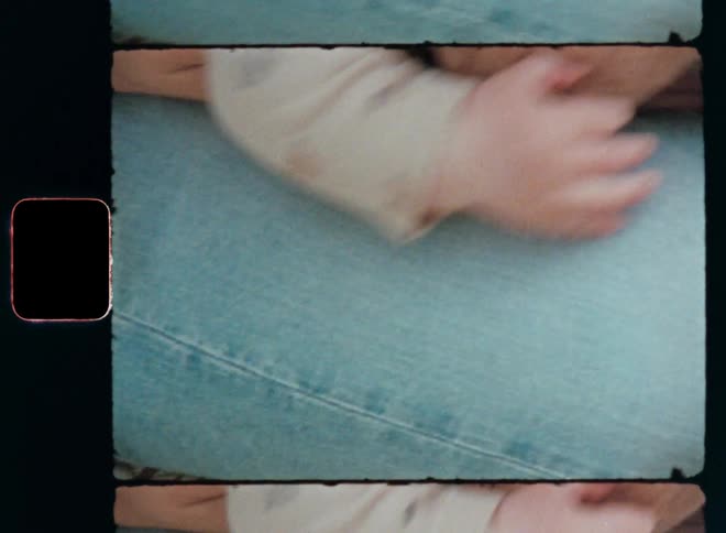 A cute baby tries to crawl over the legs of an adult wearing jeans while the infant or toddler grabs onto the lap of the caring mother that supports her trusting child on vintage 8mm film