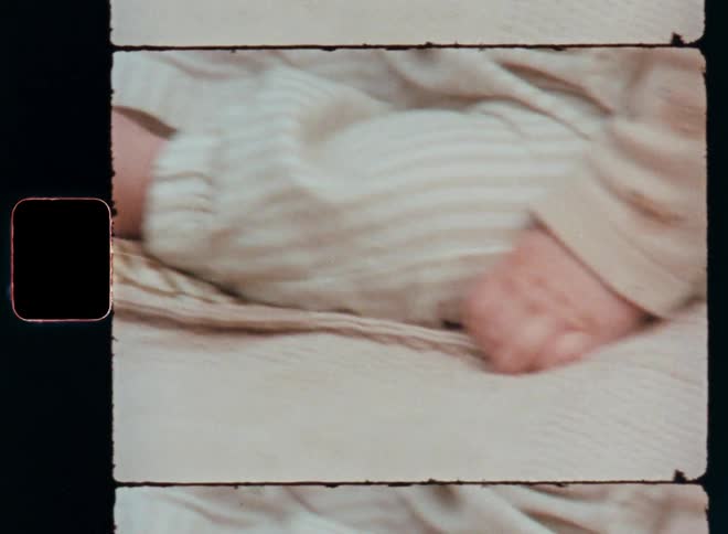 Closeup of a babys feet and hands resting in a relaxed and peaceful way on cosy and comfortable picnic blanket next to green grass enjoying a sunny spring or summer time day outside in the garden or park captured on vintage 8mm film