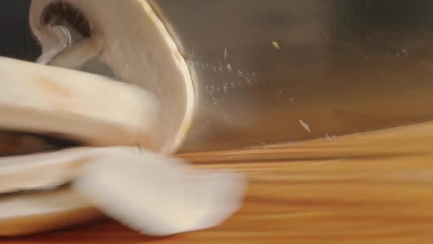 Close up of a sharp knife slicing mushrooms over a cutting table at home