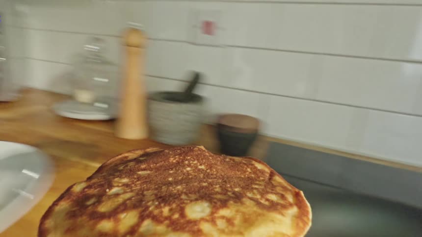 Point of view shot of a spatula picking up a pancake from a pan and placing it on a plate