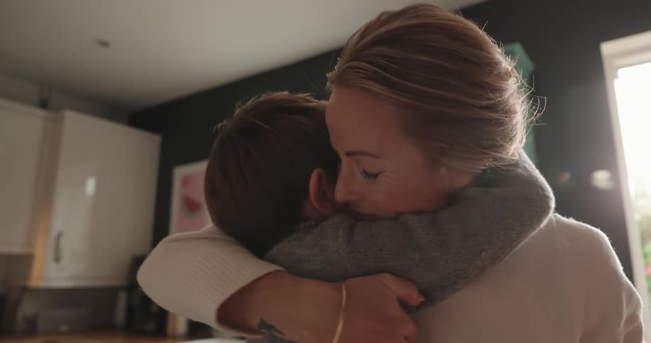 Mother and son cooking together sharing a kiss and hug in the kitchen at home