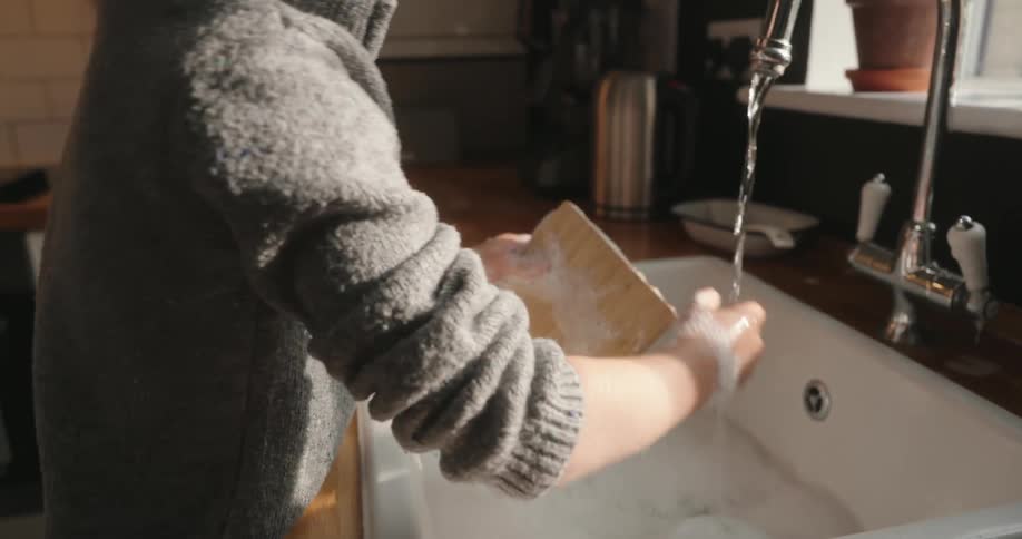 A young boy washes a cutting board in a kitchen sink