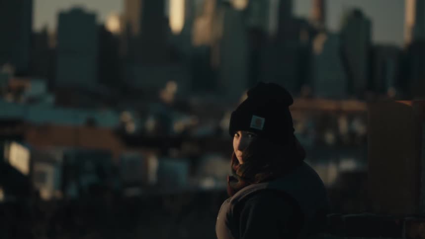 A woman in a wool cap standing near a city looks back in slow motion