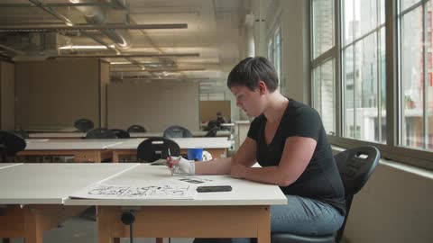 A woman sits at a table and sketches