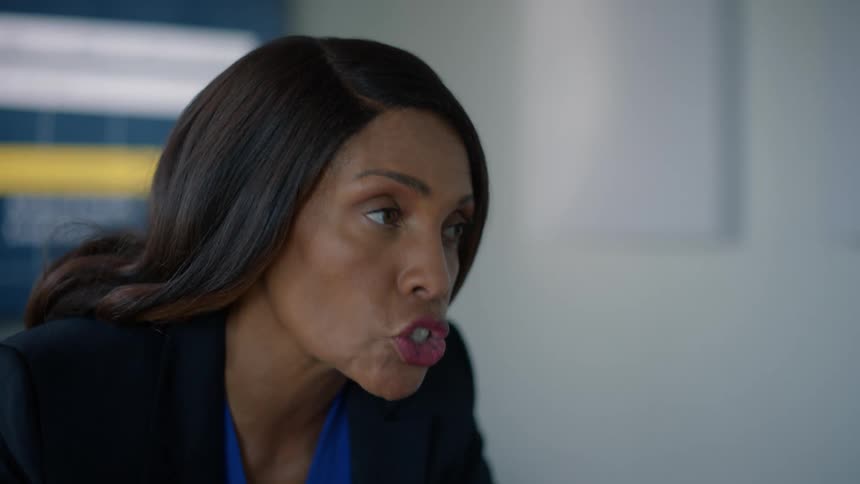A woman is talking seriously to someone in front of her and she is wearing a black blazer