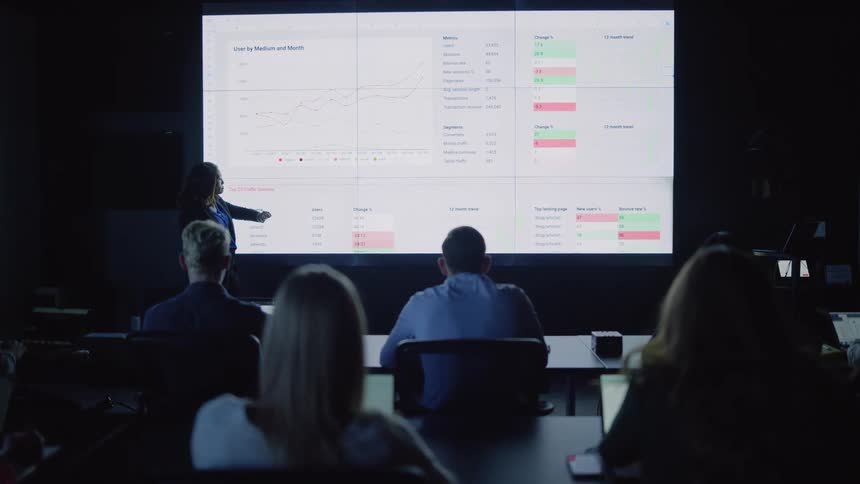 Woman standing presenting a slide in a dark auditorium to a large group