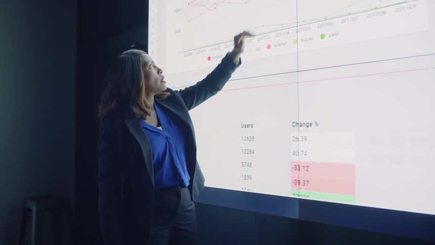 Woman in an auditorium presenting an infographic on a screen