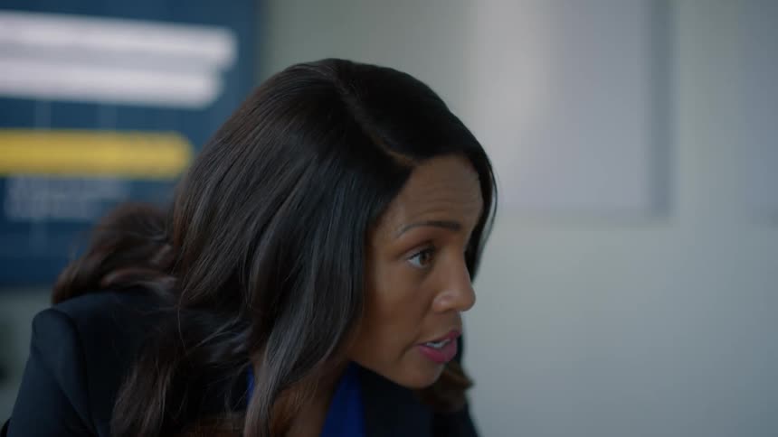 A woman wearing a black blazer and blue shirt is talking to someone standing in front of her