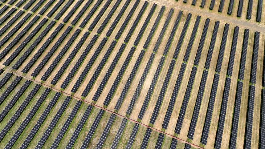 Aerial of parallel rows of solar panels filling fields at a solar farm