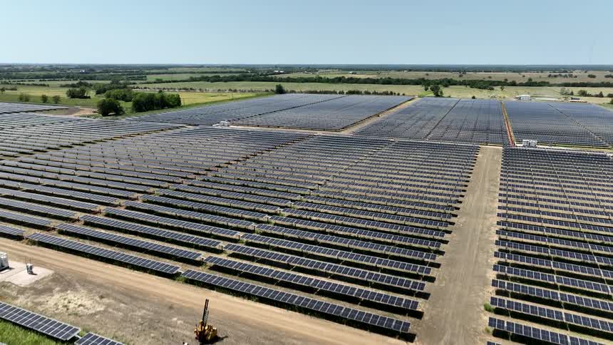 A vast solar farm stretches across a field with rows of solar panels reflecting the sunlight