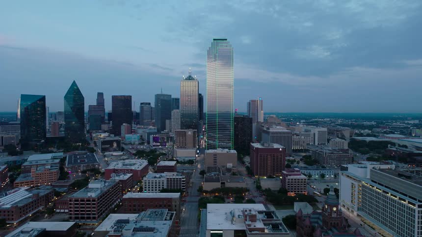 Downtown skyscrapers reflect the red tinted light on the horizon under a cloudy sky