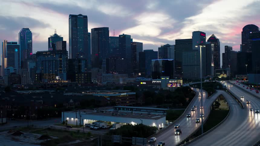 City skyline at dusk with several skyscrapers and a busy highway in the foreground