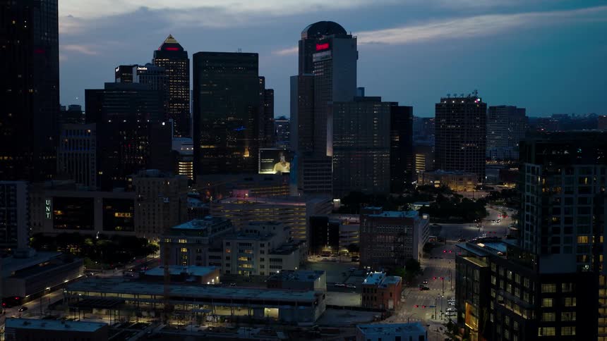 Cityscape at dusk with lights beginning to illuminate the buildings and streets creating a contrast between the darkening sky and the urban area