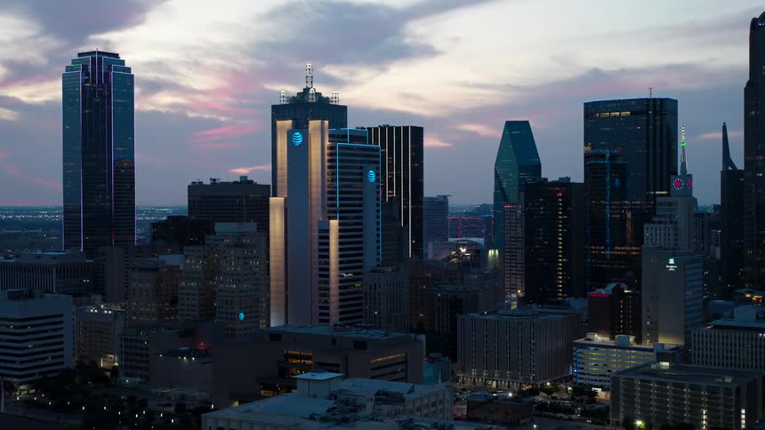 Skyline of a modern city at dusk with several skyscrapers and buildings illuminated against a twilight sky