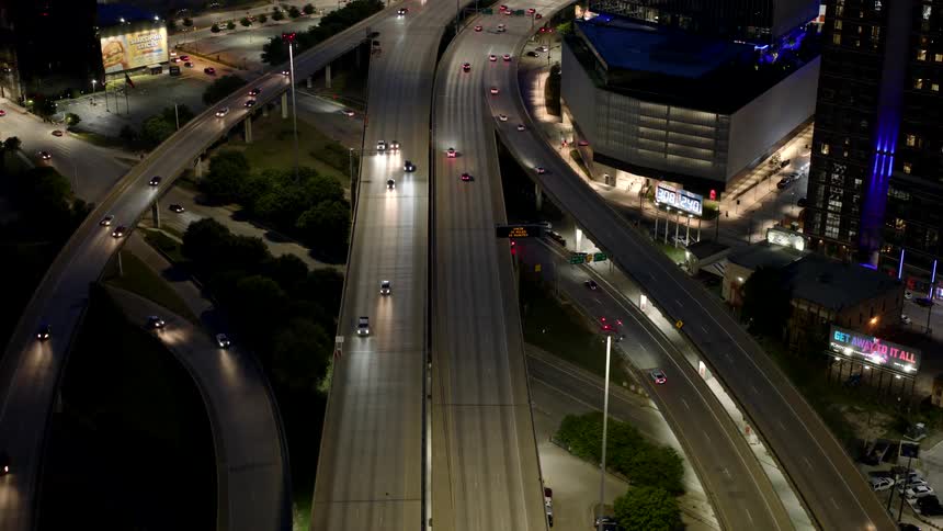 Aerial night view of a busy highway interchange with multiple lanes and merging traffic illuminated by streetlights and building lights