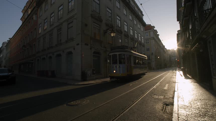 Street in a european city with a tram passing by and the sun reflecting on the horizon