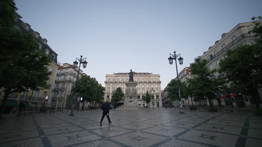 A statue stands in the center of a cobblestone square surrounded by buildings in a european cityscape