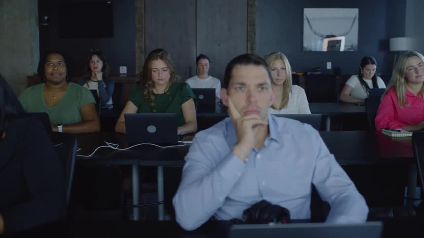 People are sitting in a meeting room and listening while using laptops