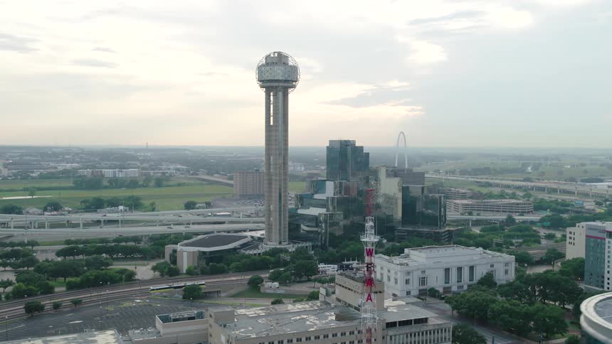 Aerial view of a city with a distinctive spherical structure atop a tower surrounded by several buildings and crisscrossing highways
