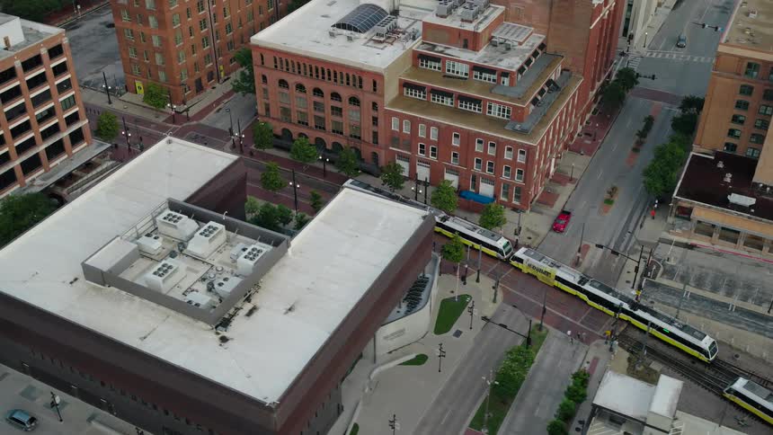 An aerial view of two white and yellow trains passing through the middle of a city with some mediumrise buildings