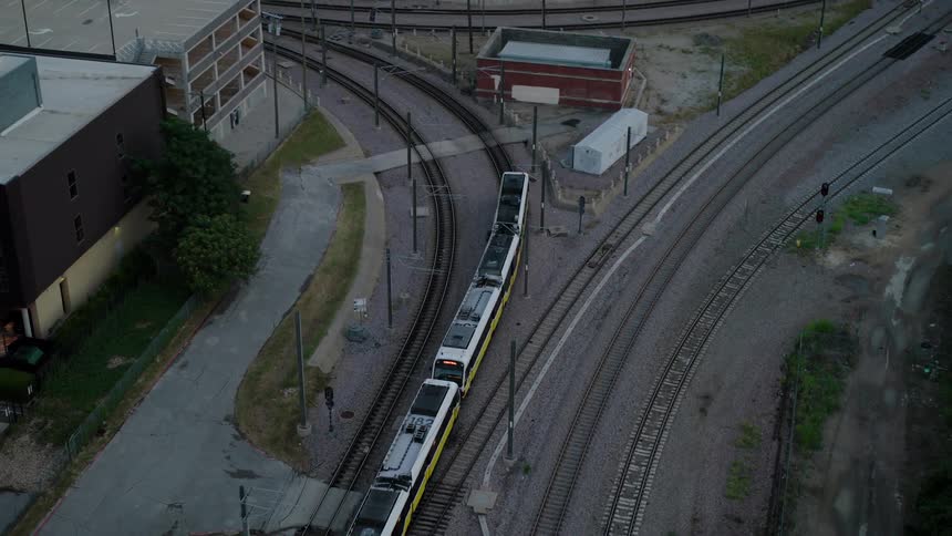 Aerial view of a train moving along a curved track through an urban area with multiple tracks and buildings surrounding the area