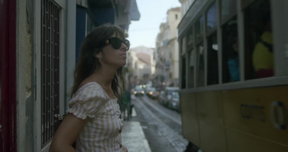 A woman standing in an old lisbon street as a tram passes by