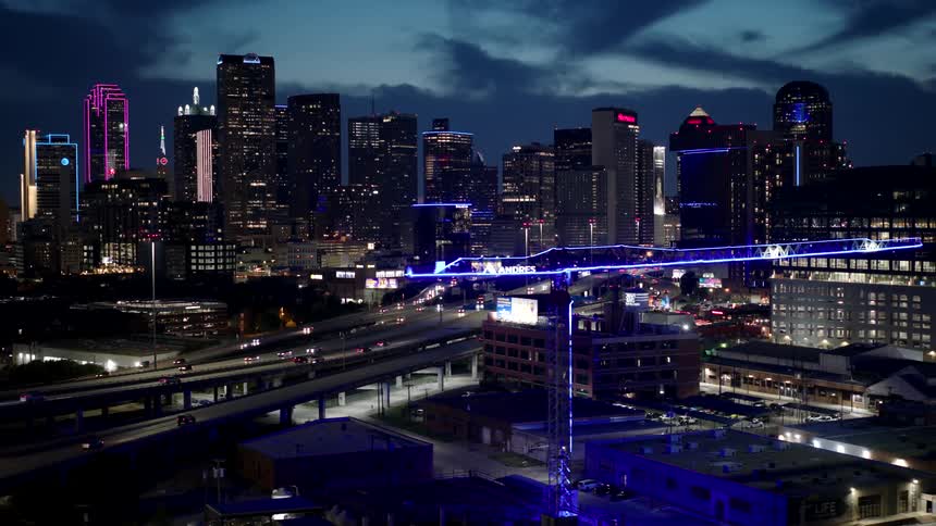 Nighttime cityscape with illuminated skyscrapers and a construction crane with blue lights