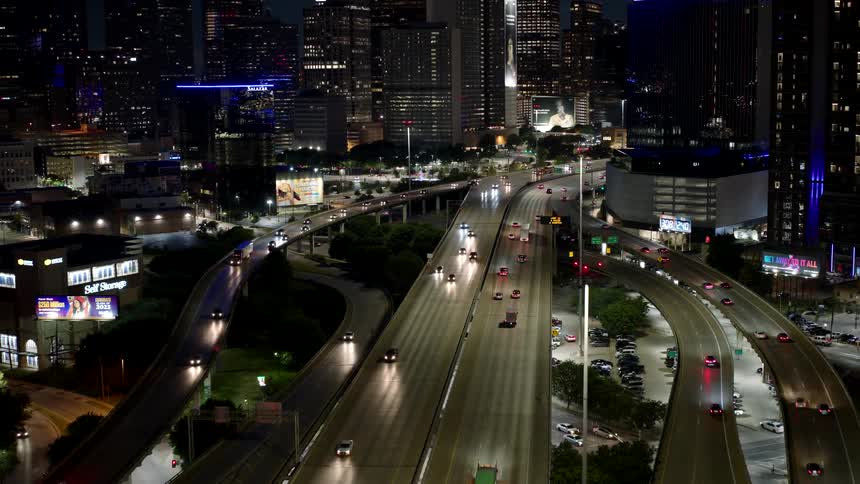 Highway and overpasses in a metropolis with vehicle traffic at night and modern buildings around