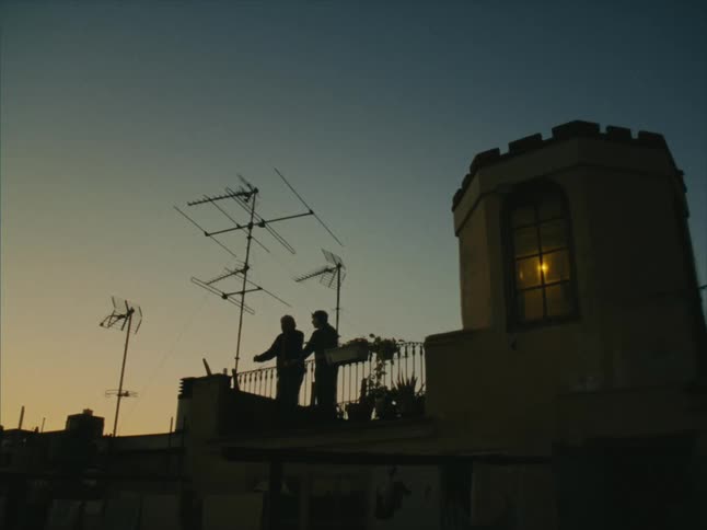Two people in silhouette stand on a balcony at dusk with the sky in shades of blue and orange