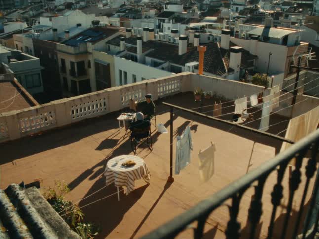 Two people sitting at a table on the terrace surrounded by buildings and clothes hanging to dry