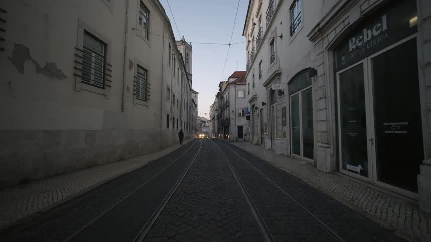 A pedestrian walks down a cramped suburban street as car headlights flicker ahead