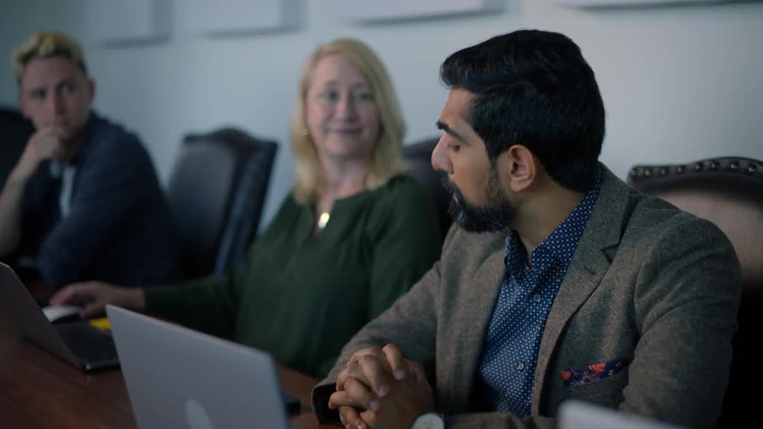People listening in an office meeting and one woman points to her coworker