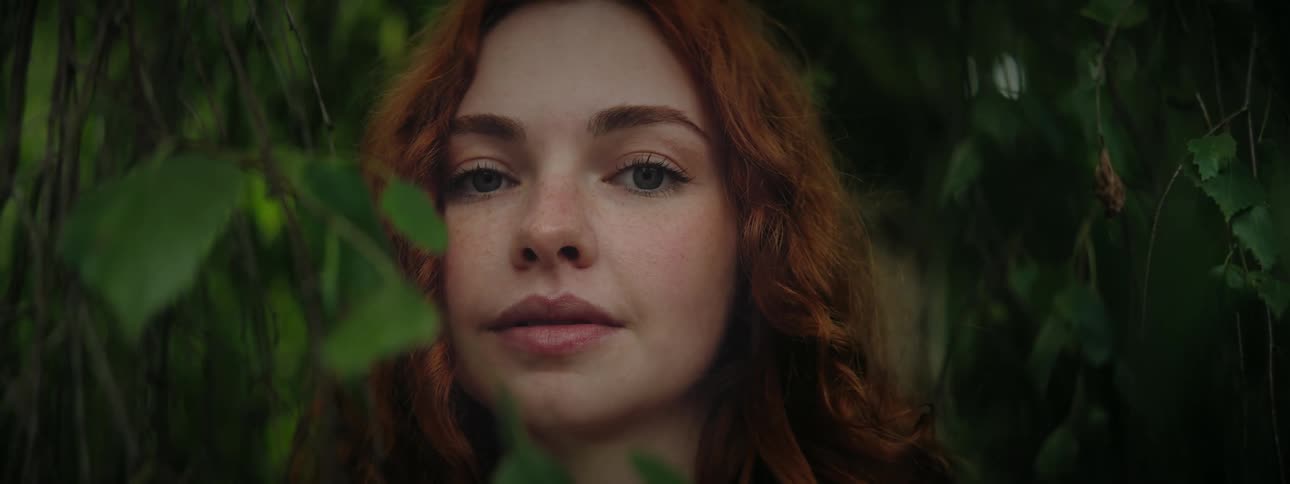 Portrait of a redhaired woman in the middle of green leaves of a tree