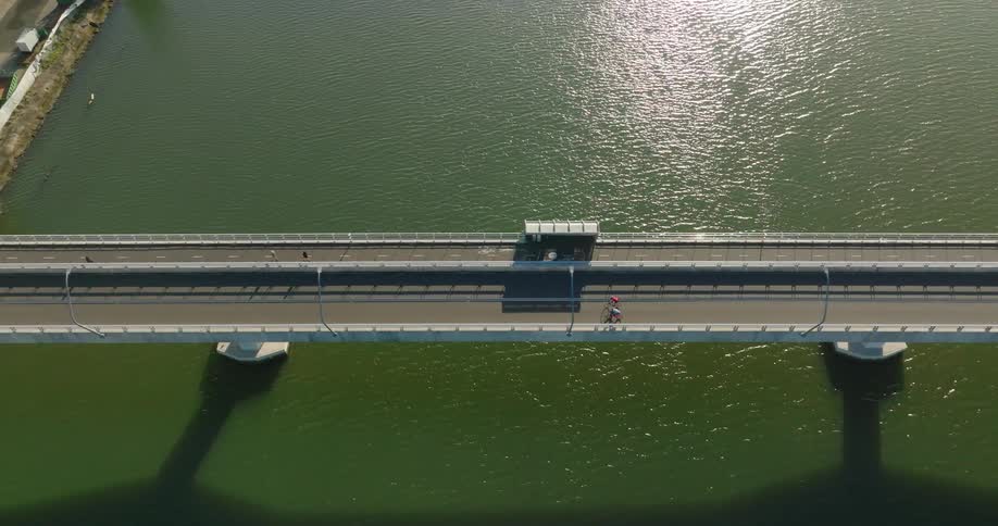 Aerial view of two cyclists riding across a bridge above a greenish sea