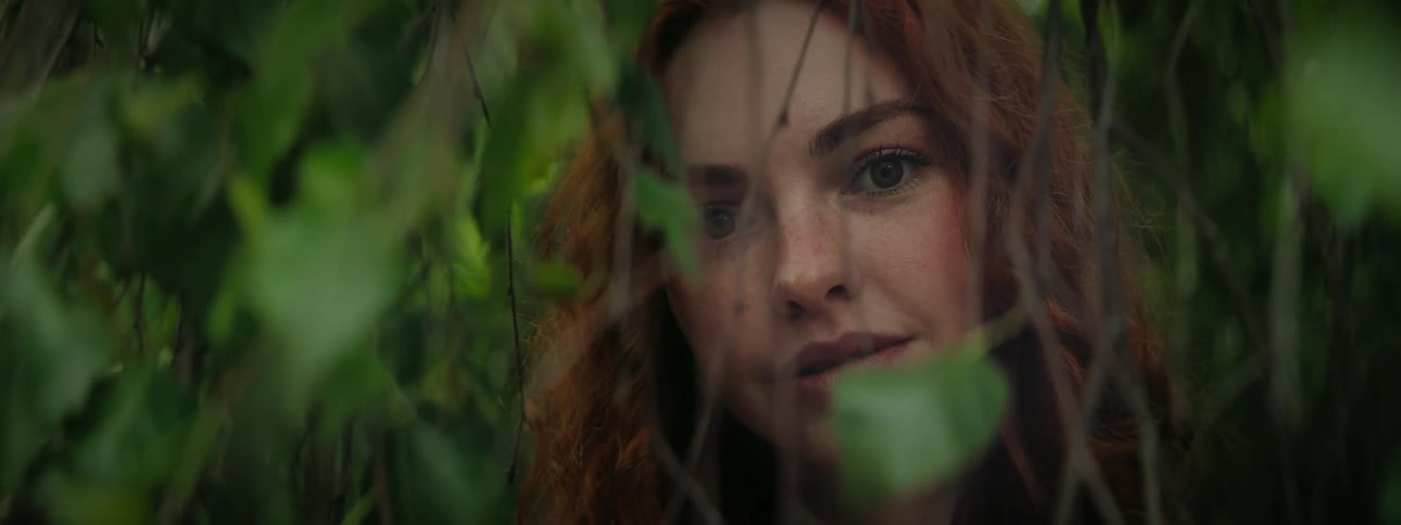 Young redhaired woman among branches and leaves of a tree