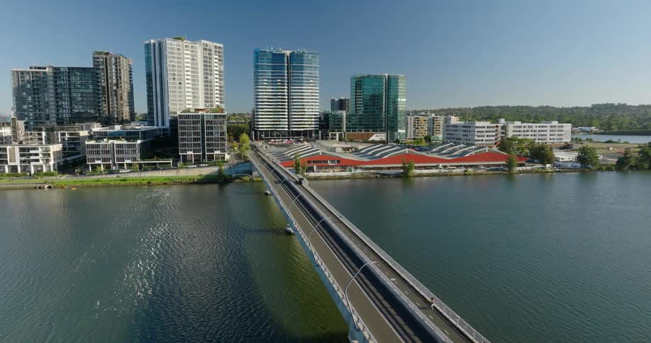 A long slender bridge stretches across a calm waterway with a modern cityscape on the other side