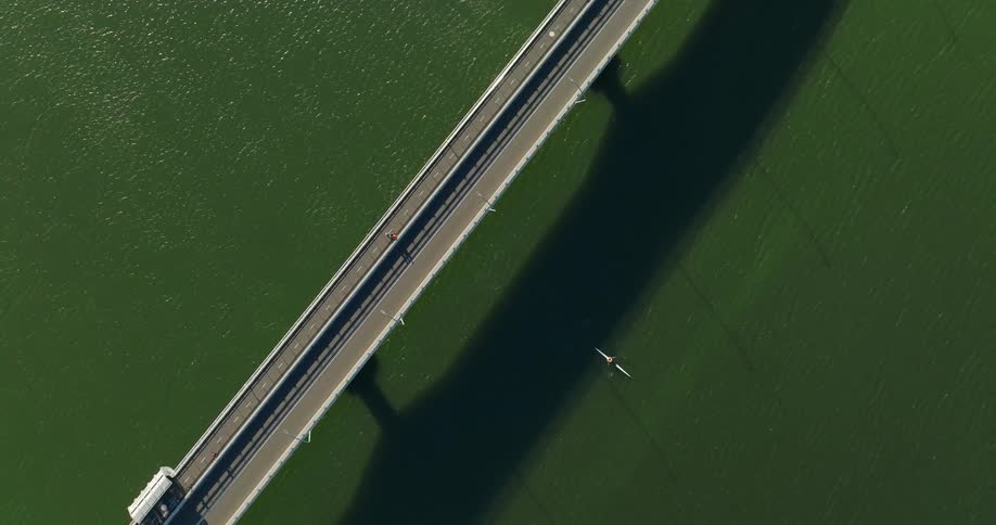Aerial view of a person paddling a kayak across a bridge in a greenish sea