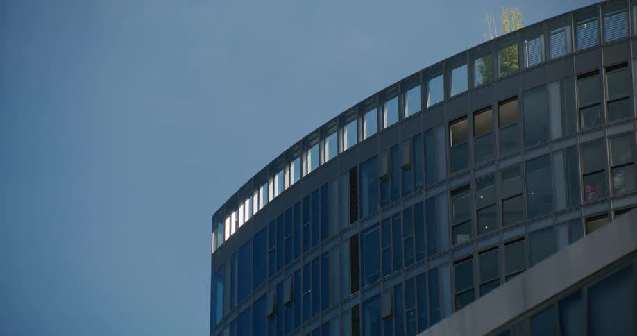 Section of a modern building with a curved facade made of reflective glass windows under a clear blue sky