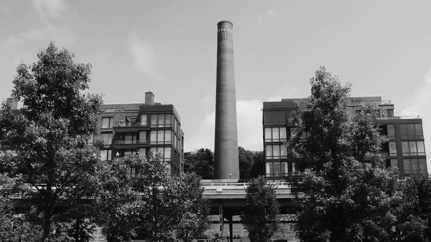 Large industrial chimney rising above a complex of buildings with trees in the foreground