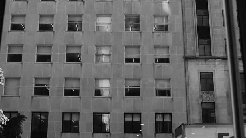 Grayscale view of a building facade with a pattern of windows some with reflections visible