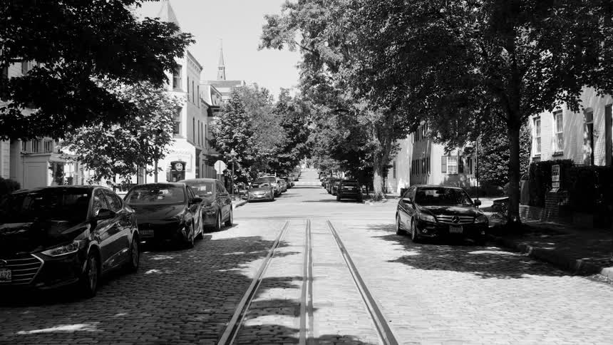 A street with a tram track in the center and some cars parked next to the sidewalks