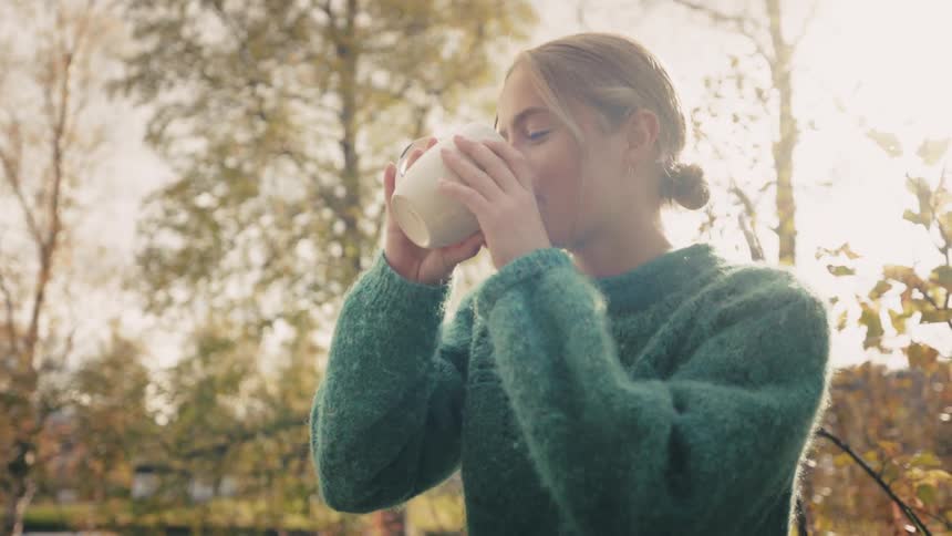 Woman standing in natural surroundings with trees around drinking a cup