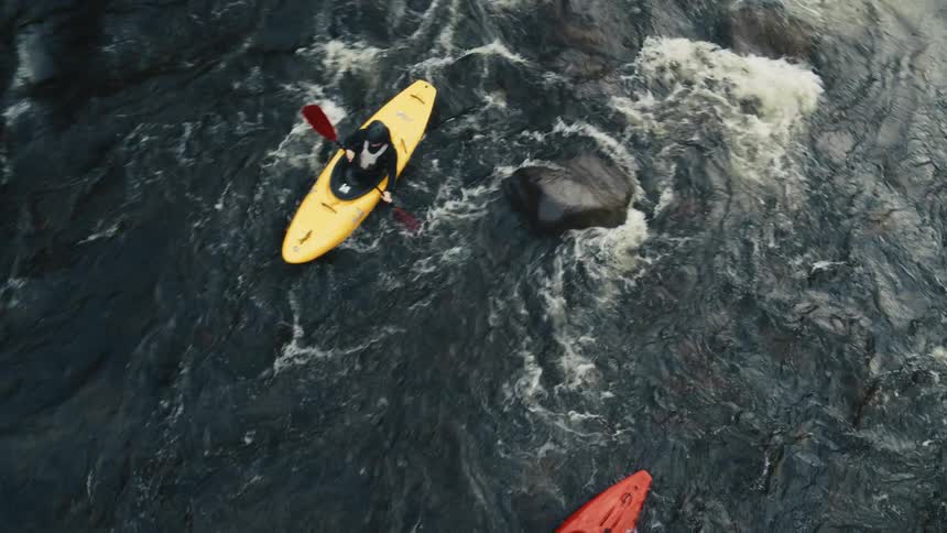 Two kayaks one yellow and one red sailing in turbulent waters