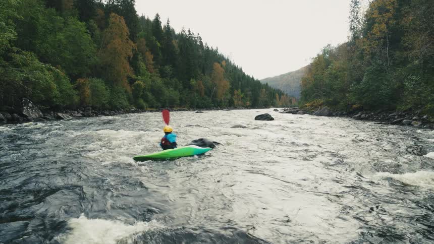 A person kayaking on a rapid river surrounded by dense forest with autumncolored foliage