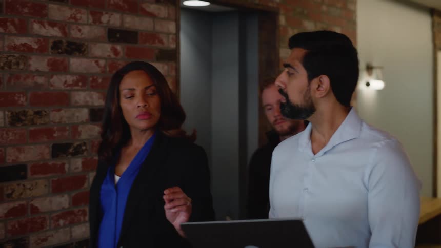 Man holding laptop and talking to two other people next to him as they walk down a hallway