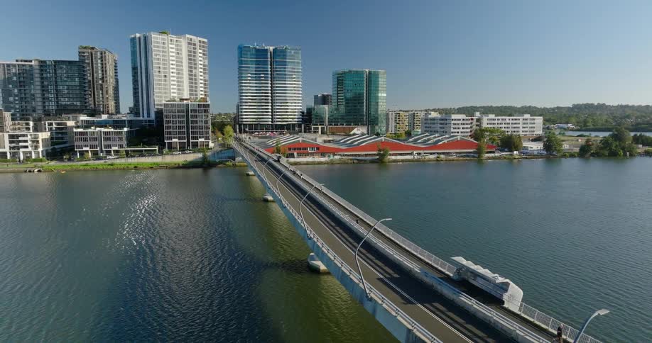 Aerial view of a modern cityscape with several skyscrapers next to a body of water and a bridge connecting two areas